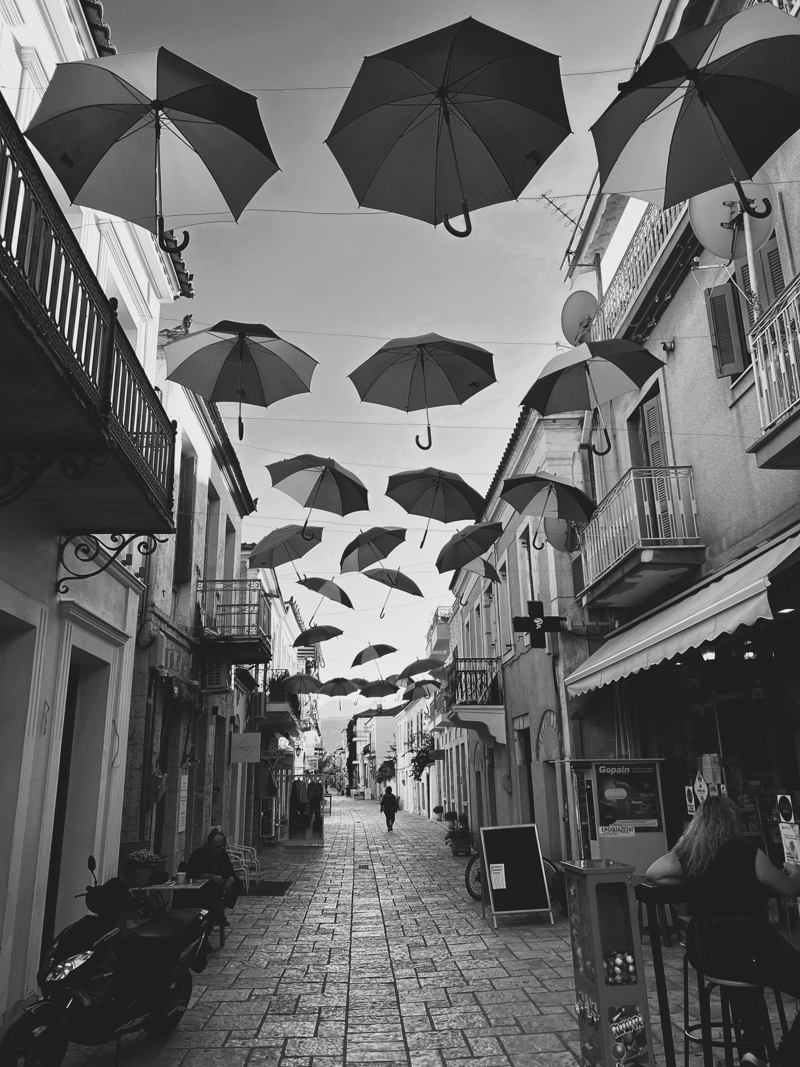 Schwarzweiss Bild einer schmalen Gasse in Griechenland mit darüber hängenden Regenschirmen